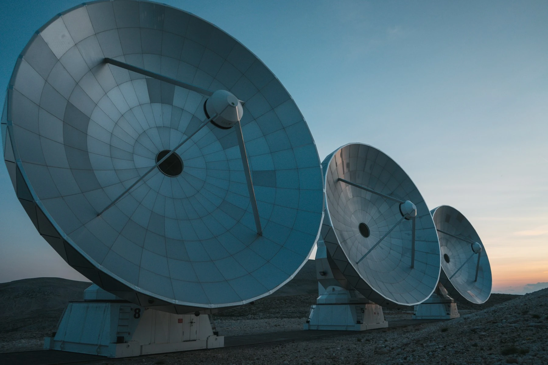 Three large radio-observatory dishes facing the sky in cool blue evening light